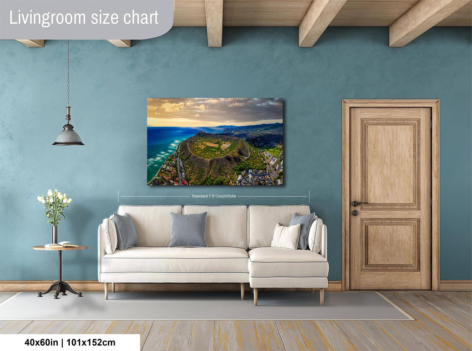 a living room with a large wall-mounted painting depicting a scenic coastal landscape. The painting is framed and hangs above a white sofa, which is positioned in front of a wooden door. The room has a wooden floor and a small table with a vase of flowers. The wall has a blue color, and the overall layout and design of the room create a cozy and inviting atmosphere.
