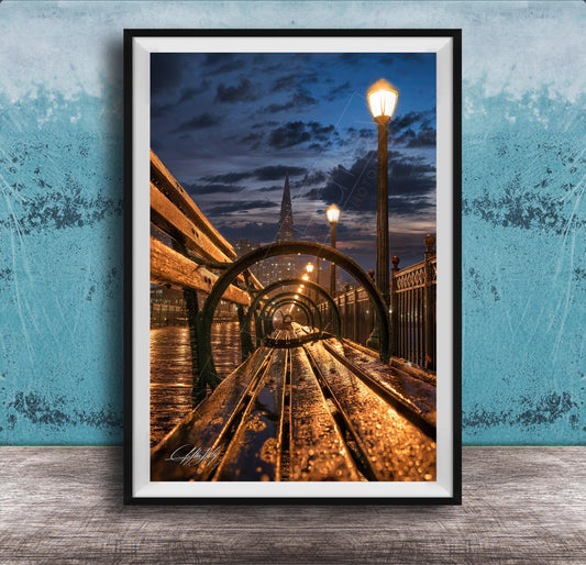 A wooden bench on a bridge at night, with a city skyline and street lamps in the background, creating a serene and atmospheric scene.