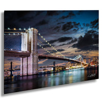A nighttime view of the Brooklyn Bridge, with its iconic towers and suspension cables illuminated against a dramatic sky.