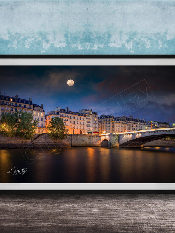 a picturesque night scene of a city with a bridge and buildings illuminated by lights, with a full moon visible in the sky.