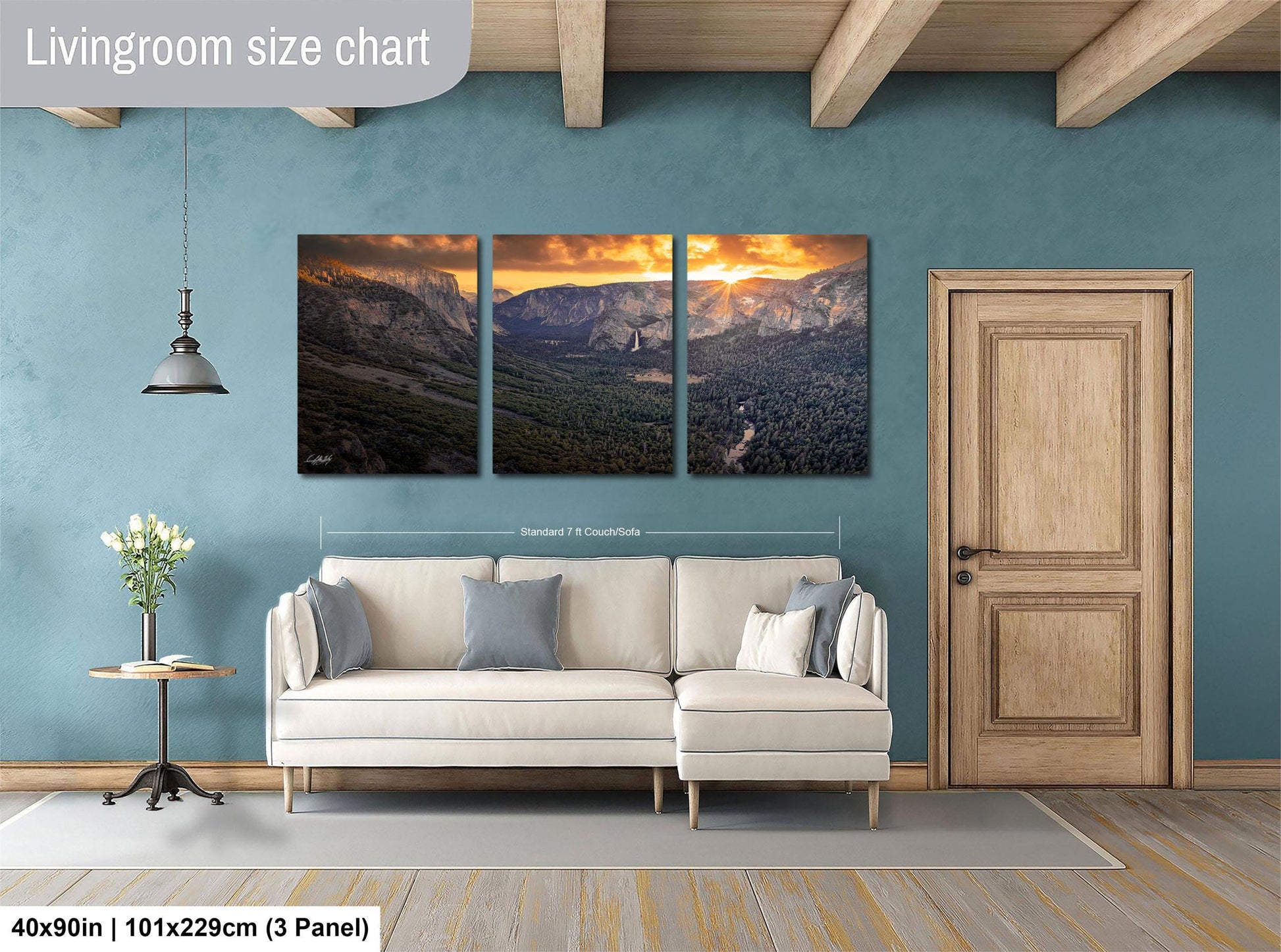 The image is a living room with a large wall-mounted painting depicting a scenic mountain landscape. The painting is divided into three panels, each showcasing different aspects of the mountain scenery. The room has a white sofa and a wooden door, creating a cozy and inviting atmosphere.