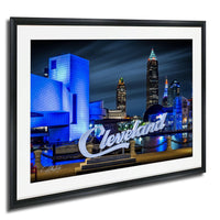 A framed photograph of the Cleveland skyline at night, with the city's iconic buildings illuminated in blue and white lights.