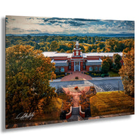 a large, red brick building with a prominent clock tower, surrounded by a lush, tree-lined landscape with a clear blue sky.
