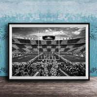 A black and white photograph of a crowded football stadium with a large audience, featuring a scoreboard and field markings.