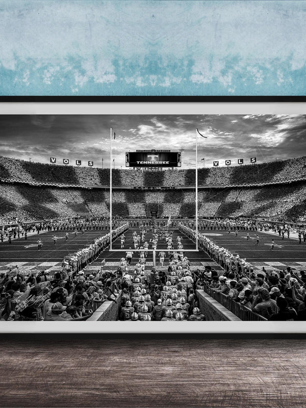 A black and white photograph of a crowded football stadium with a large audience, featuring a scoreboard and field markings.