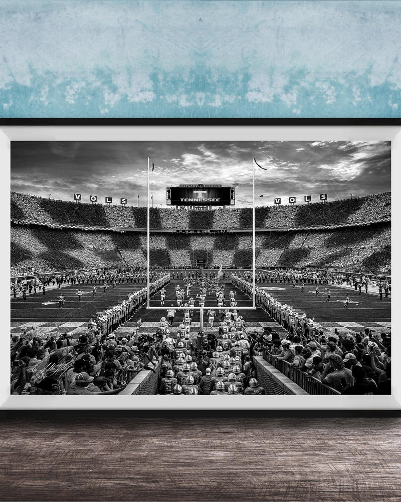 A black and white photograph of a crowded football stadium with a large audience, featuring a scoreboard and field markings.
