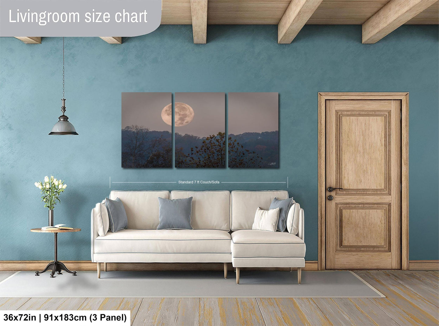 The image is a living room with a large wall art piece depicting a full moon over a landscape. The living room has a white sofa, a wooden door, and a small table with a vase of flowers. The wall art is approximately 36 inches wide and measures approximately 91 inches tall.