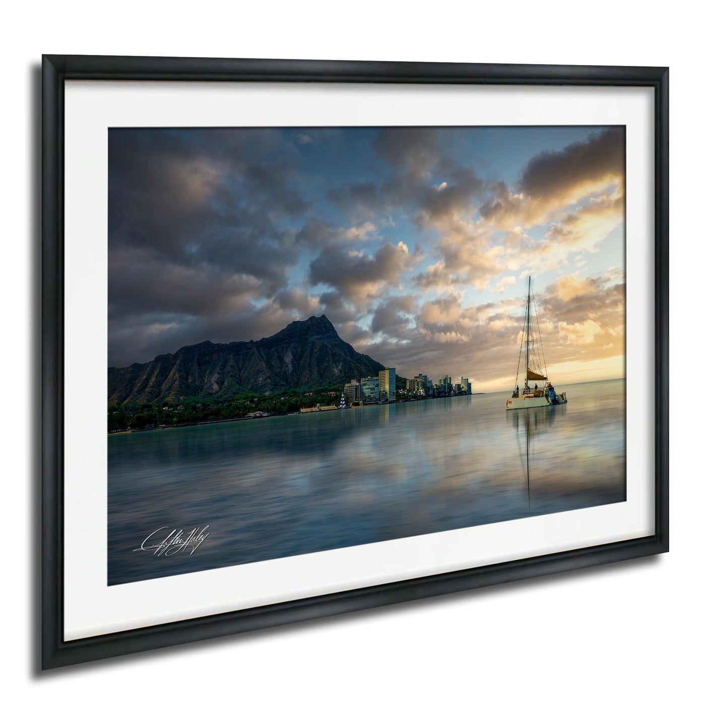 A framed photograph depicting a serene coastal scene with a sailboat on the water, a mountain range in the background, and a dramatic sky with clouds at sunset.