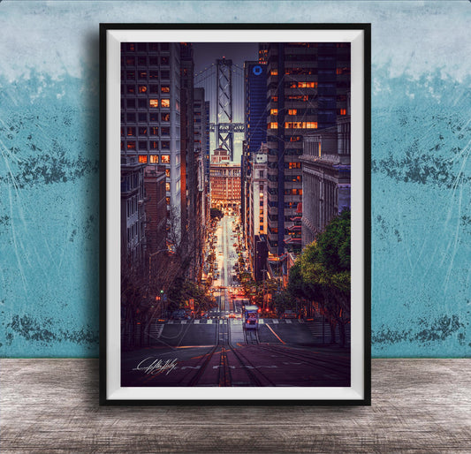 A framed photograph depicting a city street at night, with tall buildings and a bridge in the background. The street is illuminated by streetlights and the glow of the buildings, creating a vibrant and dynamic scene.