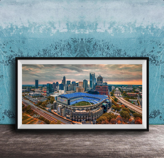 The image is a framed aerial view of a city skyline, featuring a large stadium with a distinctive blue roof.