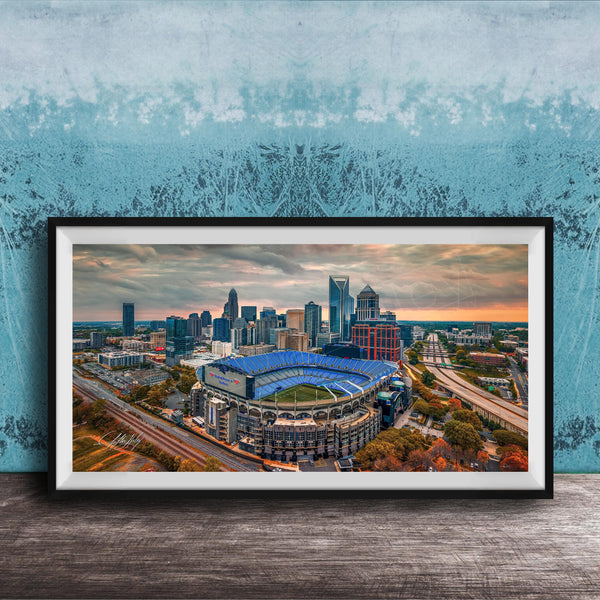The image is a framed aerial view of a city skyline, featuring a large stadium with a distinctive blue roof.