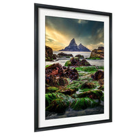 a serene landscape with a rocky shoreline, lush green vegetation, and a distant mountain range under a dramatic sky.