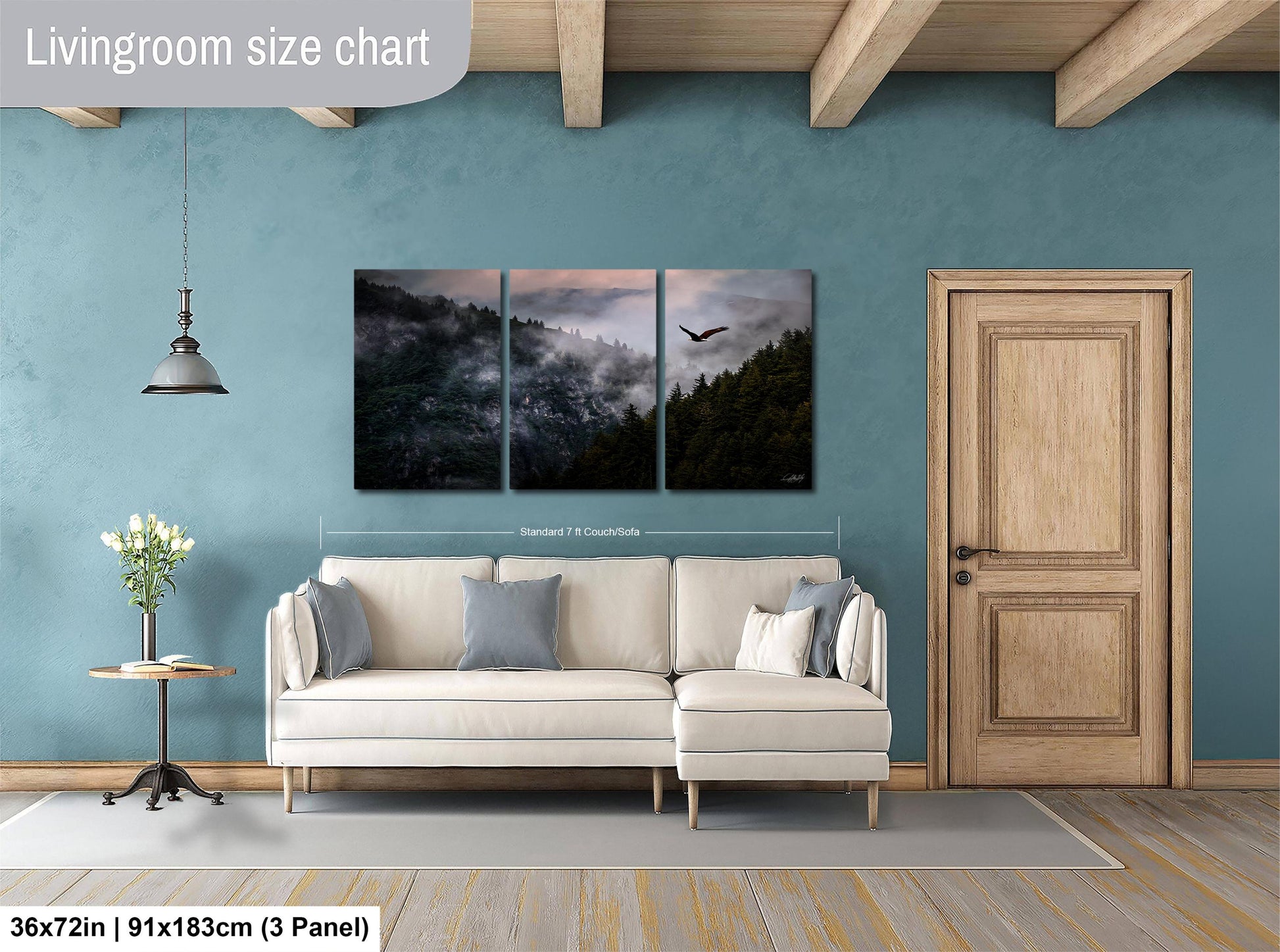 The image is a living room with a large white sofa, a wooden door, and a painting of a forest scene above it. The painting is divided into three panels, depicting a mountain landscape with a bird flying over the trees. The sofa is positioned in front of the painting, creating a cozy and inviting atmosphere in the room.