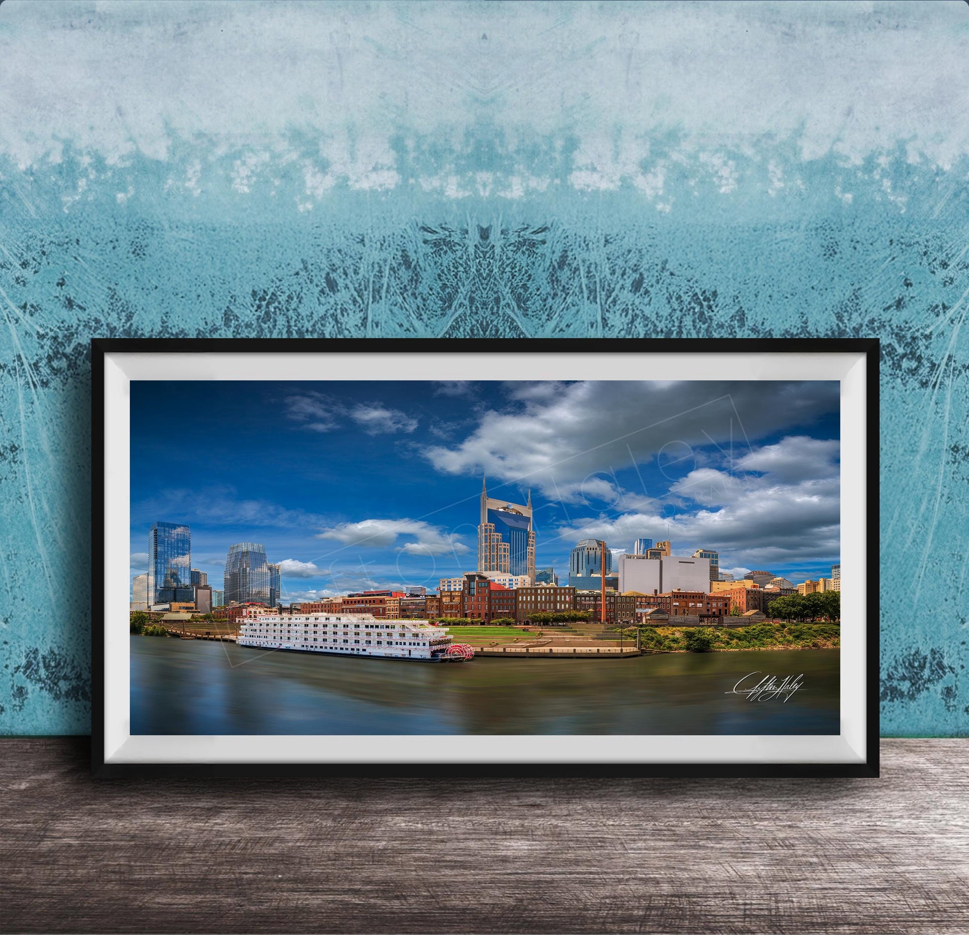 A framed photograph of a city skyline with a river in the foreground, featuring a large white boat on the water.