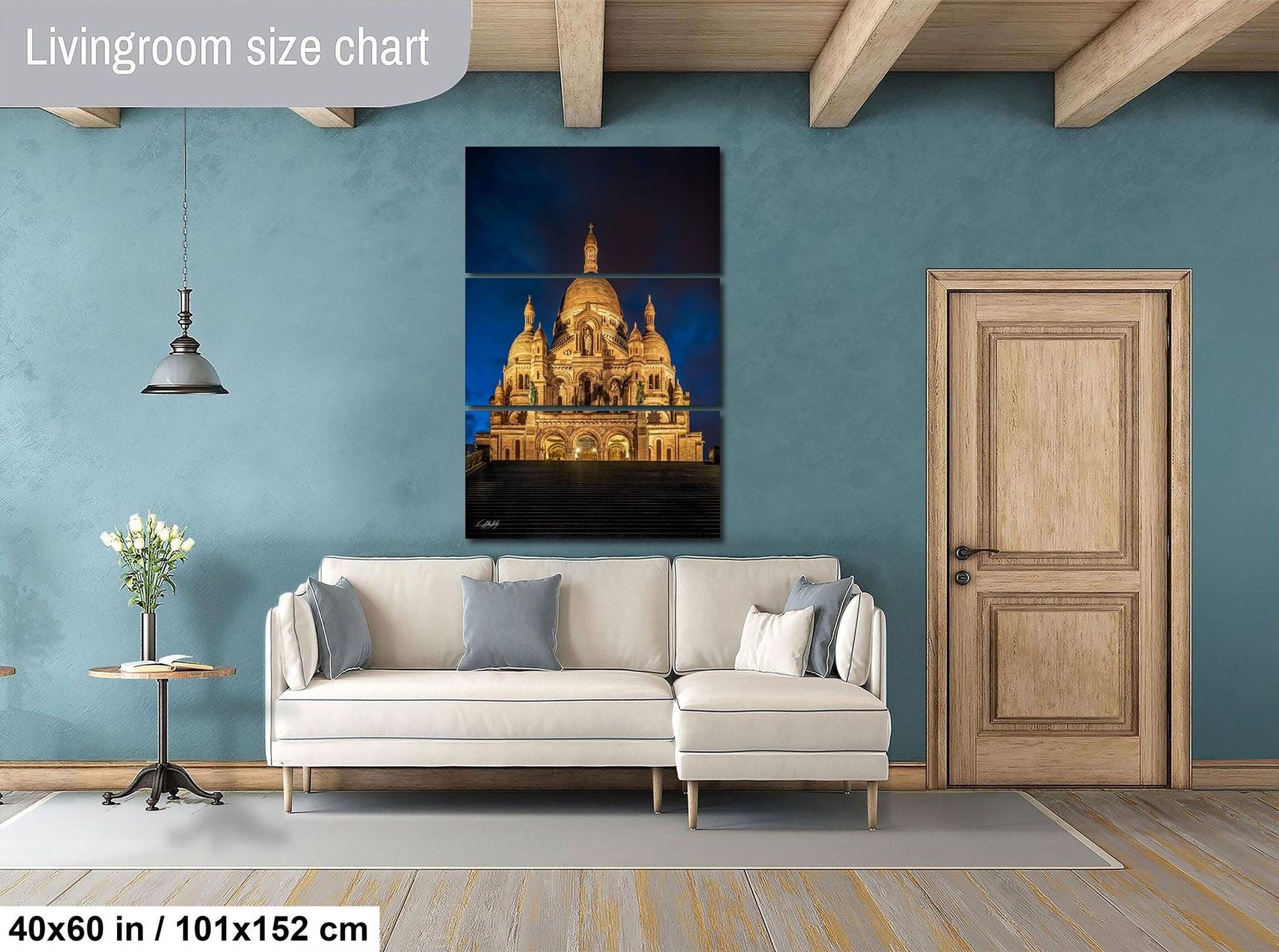 The image is a living room with a large, illuminated painting of a cathedral on the wall. The room has a white sofa, a wooden door, and a wooden table with a vase of flowers. The painting is approximately 40 inches wide and 101.5 inches tall, with a total area of 150 square inches.