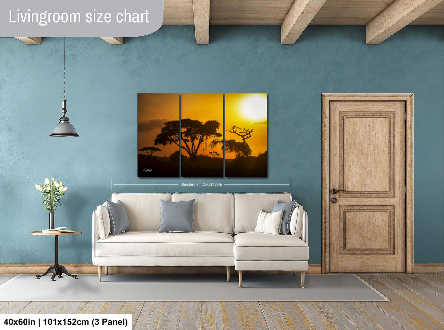 The image is a living room with a large, three-panel landscape painting hanging on the wall. The painting depicts a sunset over a field of trees. The room has a white sofa, a wooden door, and a small table with a vase of flowers. The painting is approximately 40 inches wide and 101 inches tall, with a 3-panel layout.