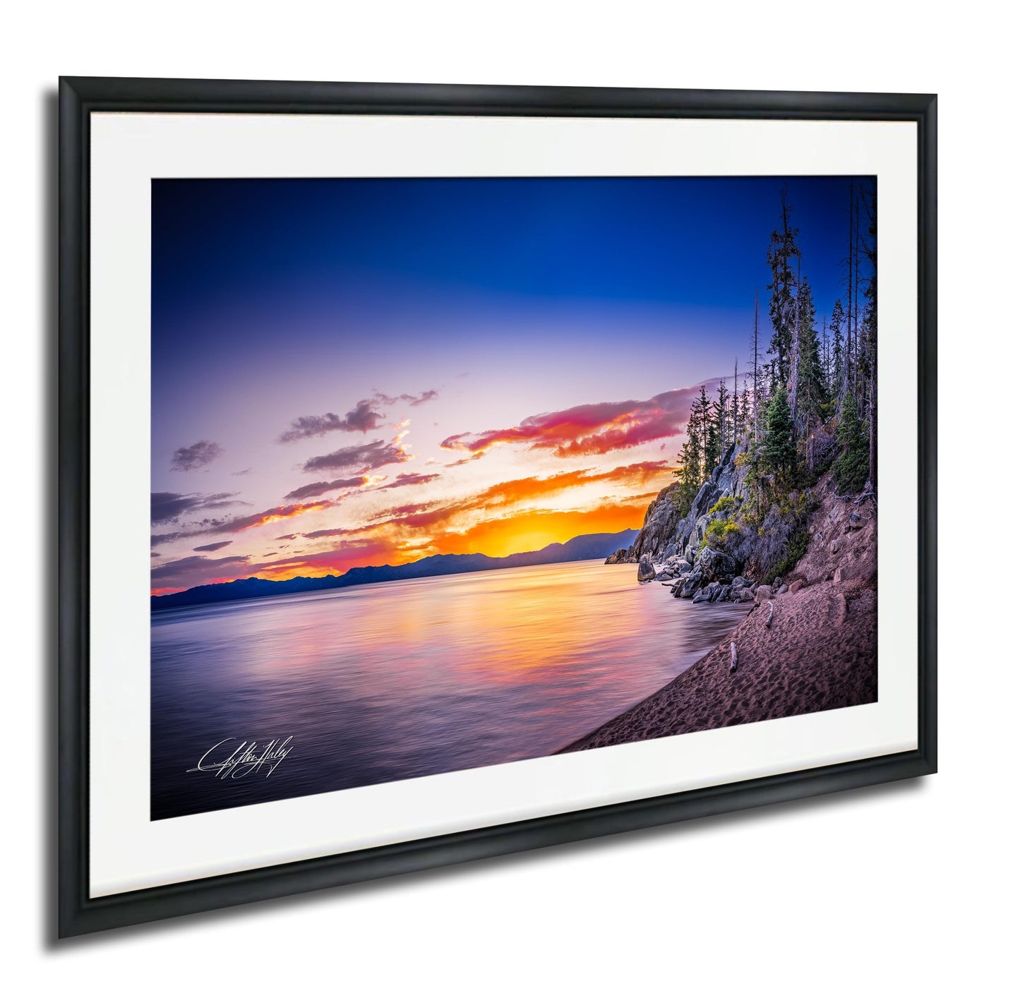 A framed photograph depicting a serene landscape with a calm lake reflecting the vibrant colors of a sunset sky, surrounded by trees and mountains.