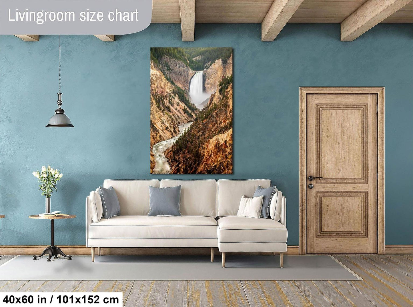 a living room with a large painting of a waterfall hanging on the wall. The painting is framed in a white frame and is approximately 40 inches wide and 51 inches tall. The room has a white sofa, a wooden door, and a wooden table with a vase of flowers. The walls are painted a light blue color, and the floor is made of wood.