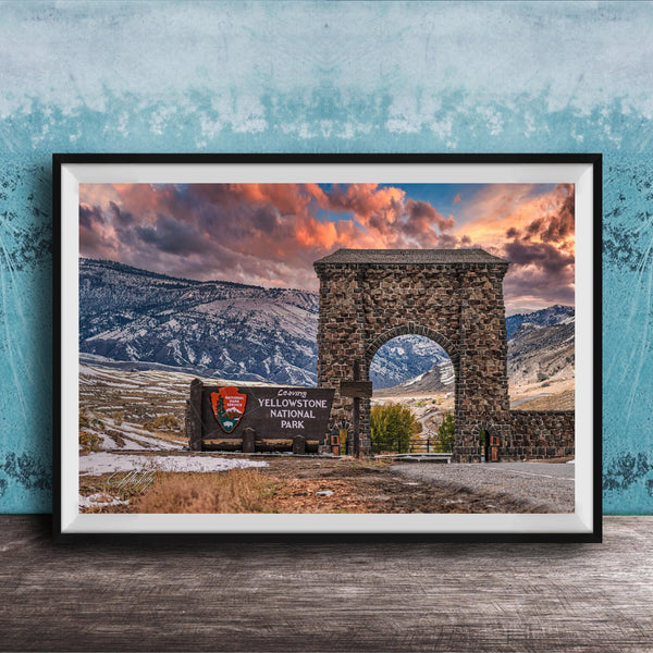 A framed photograph of the iconic Arch of the Sun, a historic stone monument located in Yellowstone National Park, with a breathtaking mountain landscape in the background.
