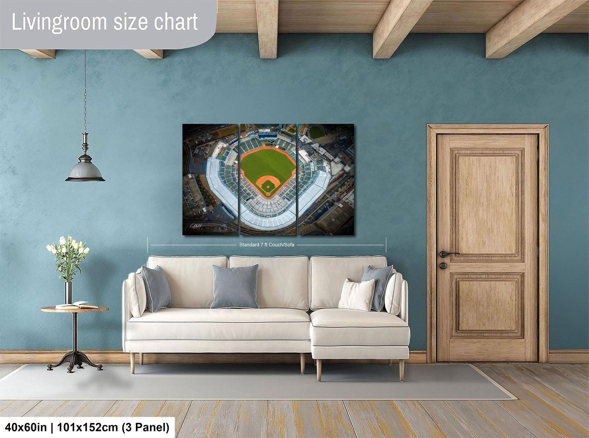 The image is a living room with a large wall-mounted poster of a baseball stadium, a white sofa, a wooden door, and a small table with a vase of flowers.