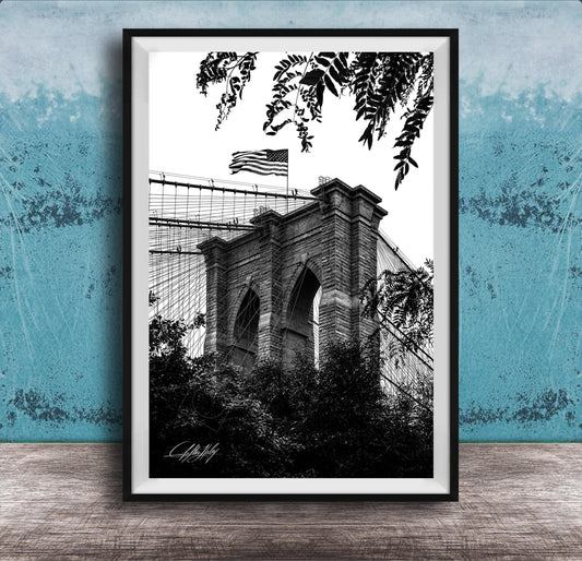 A black and white photograph of the Brooklyn Bridge, with the American flag flying atop the structure.