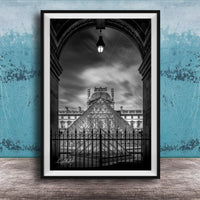 A framed black and white photograph of the Louvre Museum in Paris, France, with the iconic glass pyramid structure of the museum prominently featured.