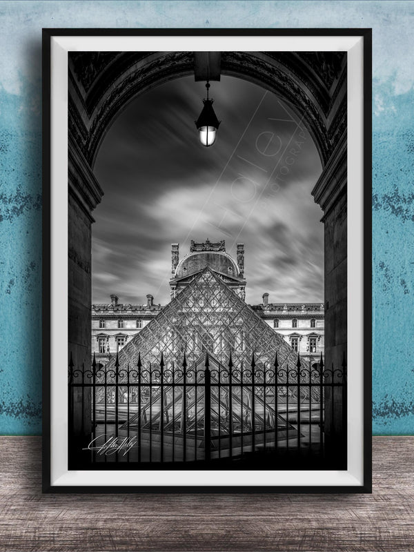 A framed black and white photograph of the Louvre Museum in Paris, France, with the iconic glass pyramid structure of the museum prominently featured.