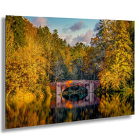 A picturesque stone bridge spanning a tranquil lake, surrounded by a vibrant autumn landscape with trees displaying a mix of yellow, orange, and green foliage.
