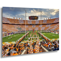 a large crowd of people wearing orange clothing gathered in a stadium, with a football field visible in the background.