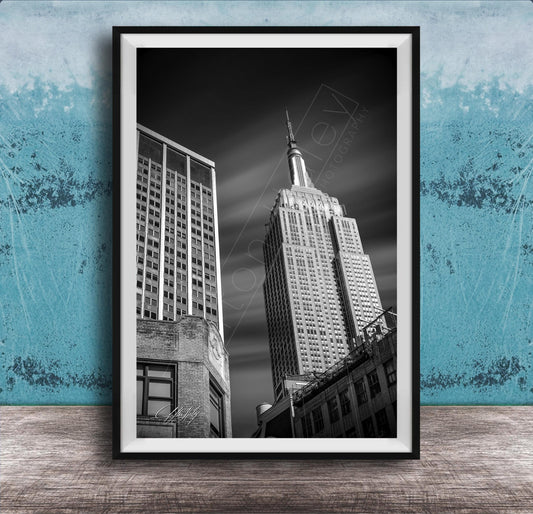 A black and white photograph of the Empire State Building, a famous skyscraper in New York City, with a blue wall in the background.