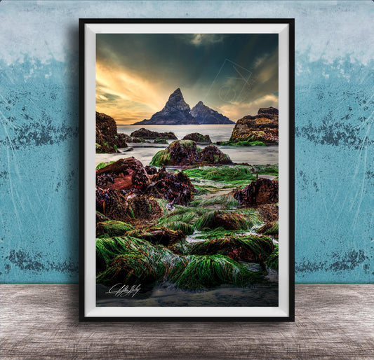 The image is a framed photograph of a rocky shoreline with a large, distant mountain in the background. The photograph is set against a blue wall, and the sky above is cloudy. The image is a collage of multiple images, and the photograph is framed with a black border.