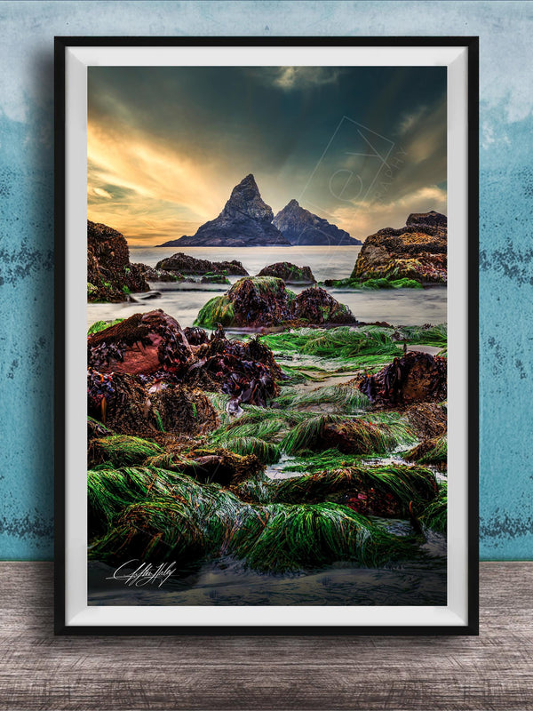The image is a framed photograph of a rocky shoreline with a large, distant mountain in the background. The photograph is set against a blue wall, and the sky above is cloudy. The image is a collage of multiple images, and the photograph is framed with a black border.