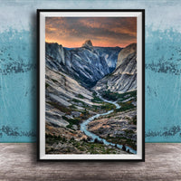 The image is a framed photograph of a mountainous landscape with a winding river, set against a backdrop of a dramatic sky with clouds and a sunset.