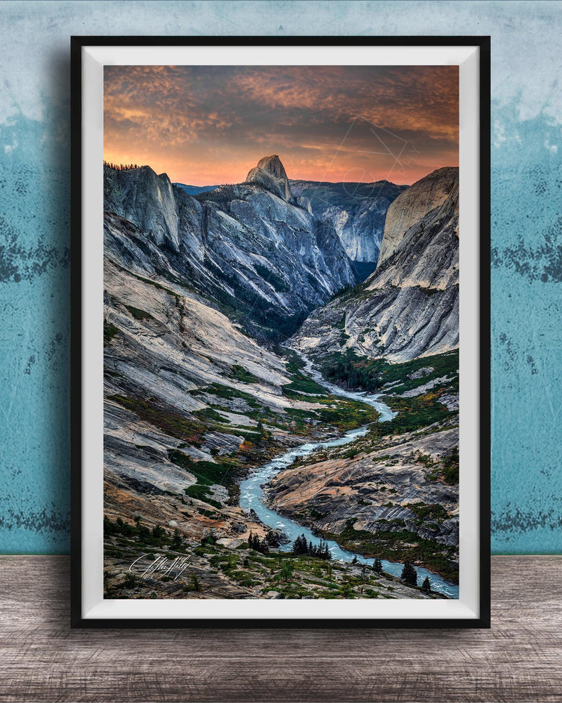 The image is a framed photograph of a mountainous landscape with a winding river, set against a backdrop of a dramatic sky with clouds and a sunset.