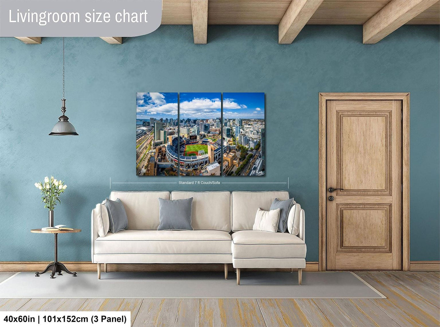 The image is a living room with a large, high-resolution painting of a cityscape hanging on the wall. The painting is divided into three panels, depicting a panoramic view of the city. The room has a white sofa, a wooden door, and a small table with a vase of flowers. The painting is approximately 40 inches wide and 101.5 inches tall, with a 3-panel layout.
