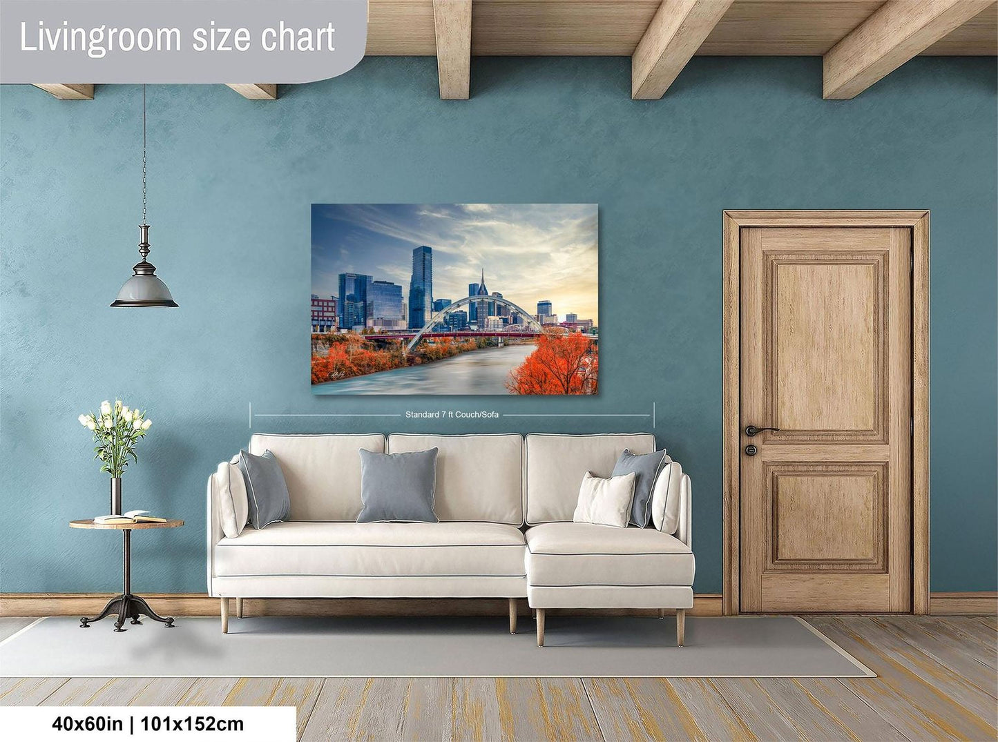 a living room with a large wall painting depicting a city skyline, a white sofa, a wooden door, and a small table with a vase of flowers.
