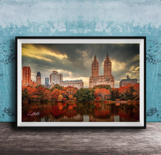 a cityscape with tall buildings and a lake in the foreground, surrounded by trees with autumn foliage.