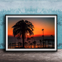 A framed photograph depicting a palm tree silhouetted against a vibrant sunset over the ocean.