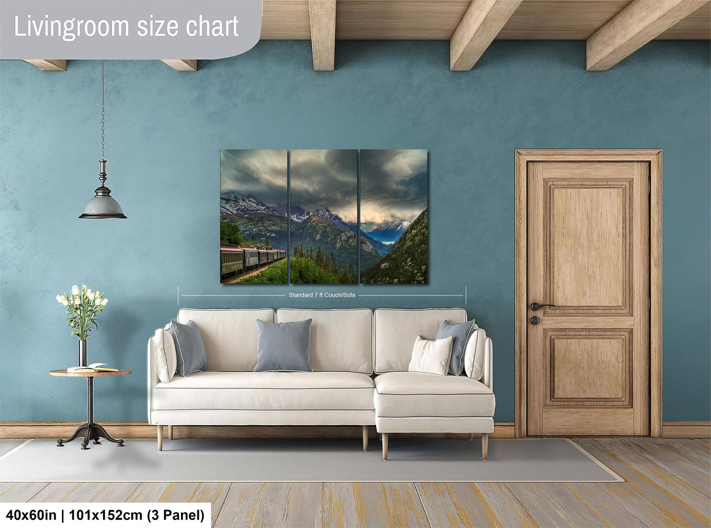The image is a living room with a large, high-quality landscape painting hanging on the wall. The painting depicts a scenic mountain view with a train passing through the landscape. The room is furnished with a white sofa and a wooden door, creating a cozy and inviting atmosphere. The painting is approximately 40 inches wide and 101.5 inches tall, making it a prominent feature in the room.