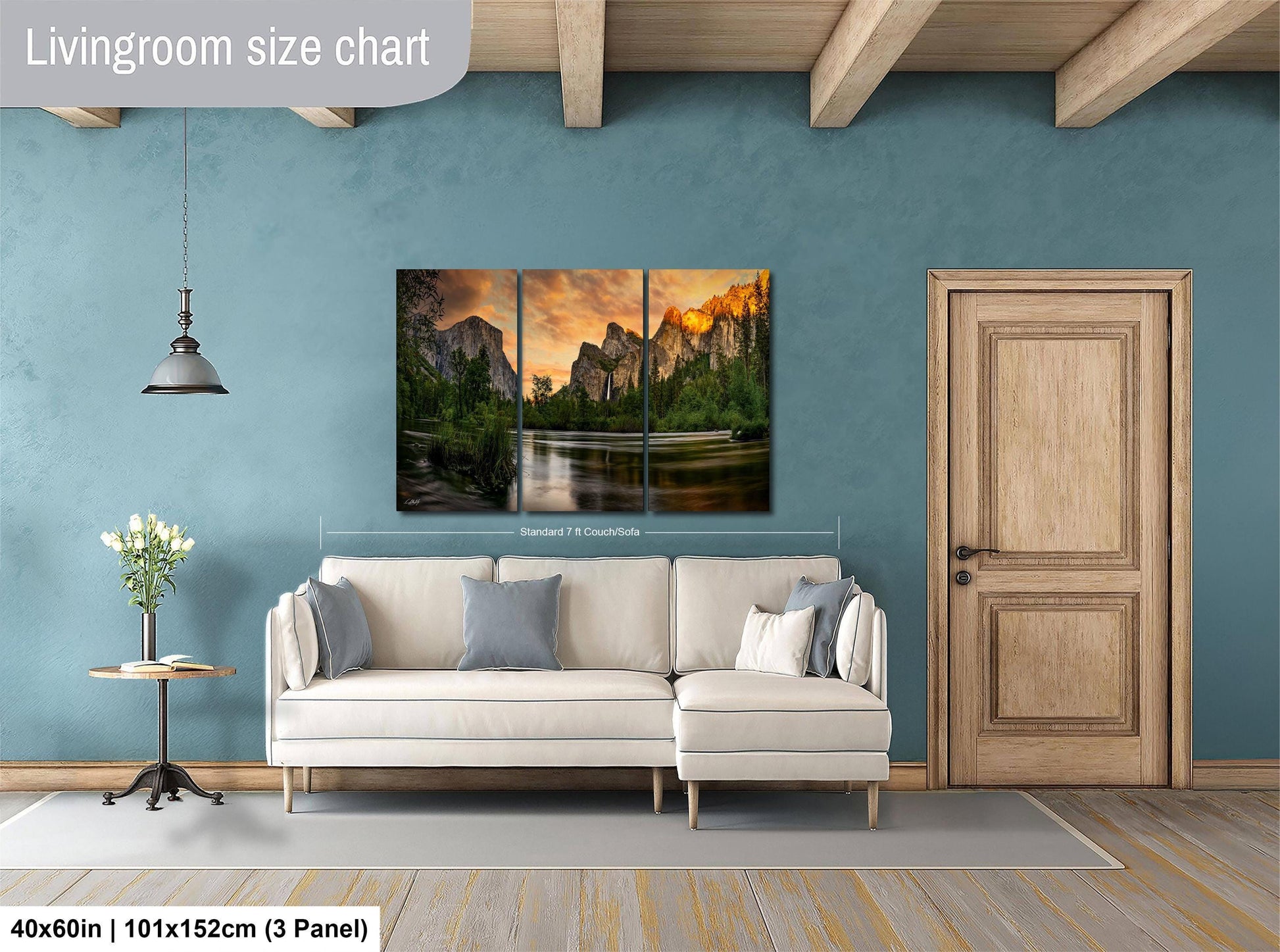 The image is a living room with a large, three-panel landscape painting hanging on the wall. The painting depicts a scenic mountain landscape with a river and a sunset. The room has a white sofa and a wooden door, creating a cozy and inviting atmosphere.