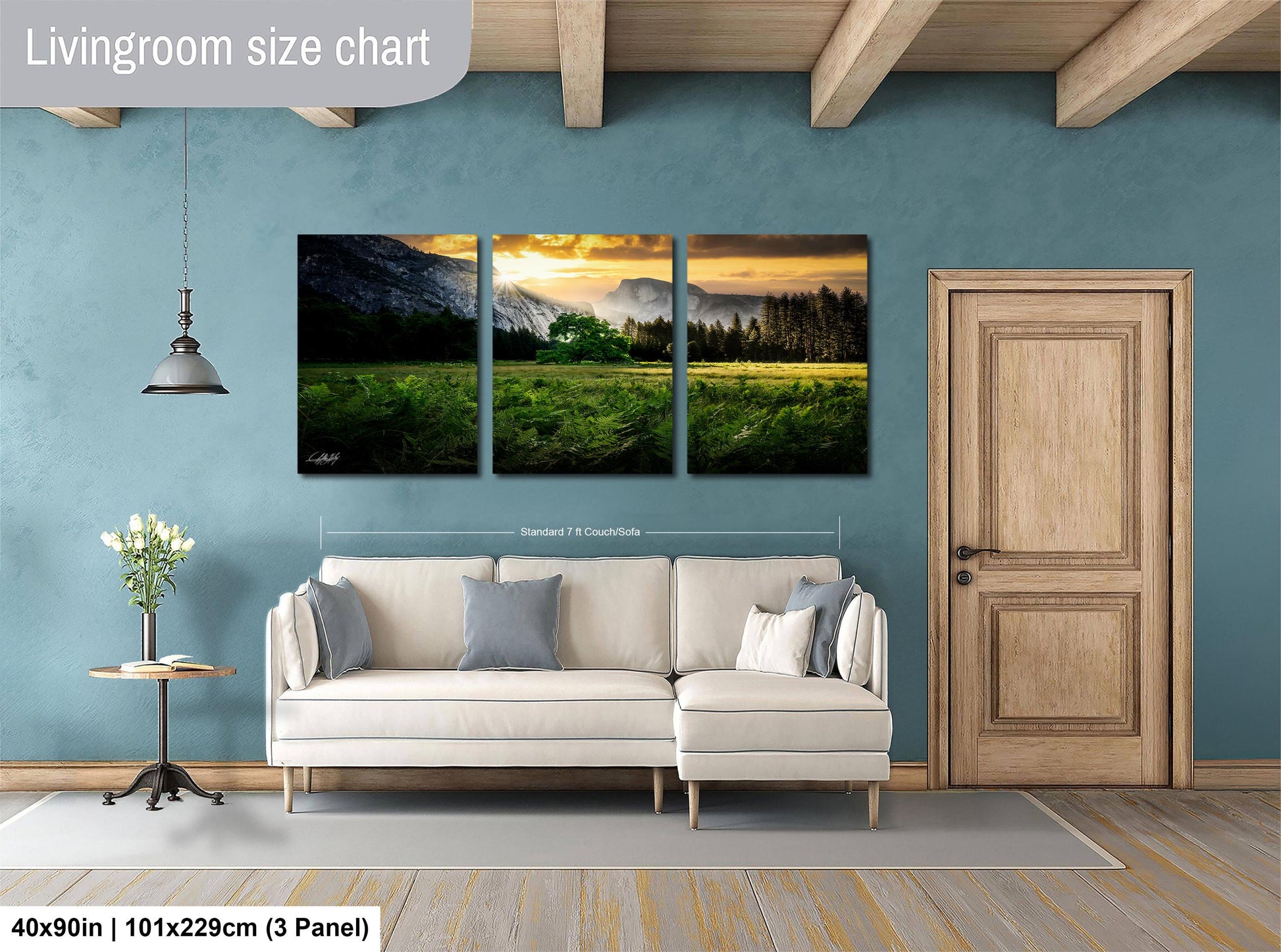 The image is a living room with a large, three-panel landscape painting hanging on the wall. The painting depicts a serene mountain landscape with a sunset over the mountains. The room is furnished with a white sofa and a wooden door, creating a cozy and inviting atmosphere.