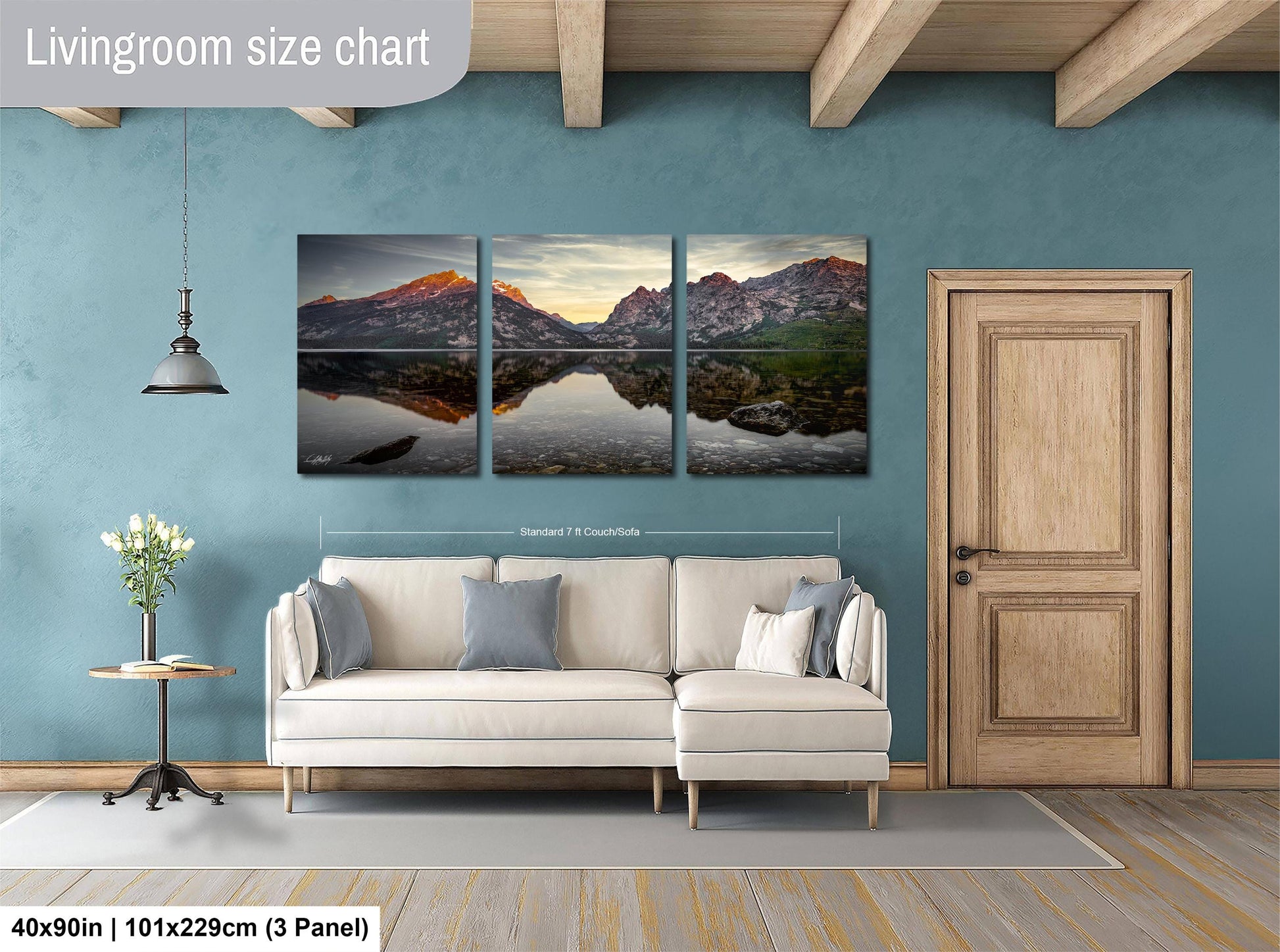 The image is a living room with a large wall art depicting a scenic landscape with mountains and a lake. The wall art is divided into three panels, each showing a different part of the landscape. The room has a white sofa, a wooden door, and a small table with a vase of flowers. The living room size chart indicates that the wall art is approximately 40 inches wide and 101.29 cm tall, with a 3-panel layout.