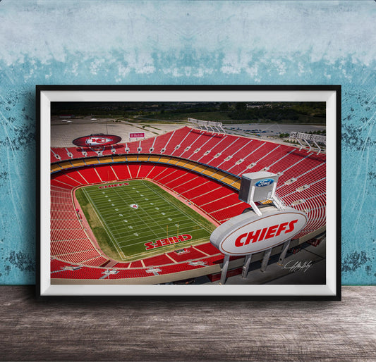 The image is a framed photograph of a football stadium, specifically the Kansas City Chiefs stadium, with the team's logo prominently displayed on the field.