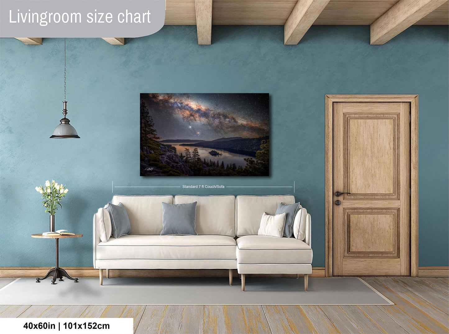a living room with a large wall painting of a serene landscape featuring a lake and mountains. The painting is hung above a white sofa, which is positioned on a gray rug. The room has a wooden door and a small table with a vase of flowers. The wall painting is approximately 40 inches wide and 115 centimeters tall.
