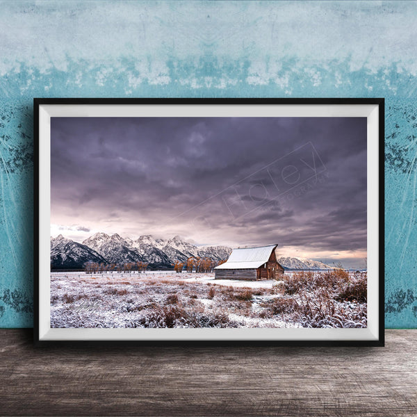 A framed photograph depicting a snowy mountain landscape with a wooden barn in the foreground, set against a cloudy sky.