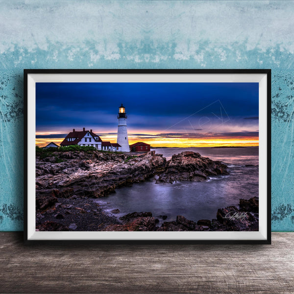 A framed photograph depicting a lighthouse on a rocky shore at sunset, with the sky filled with vibrant colors and the ocean reflecting the warm hues.