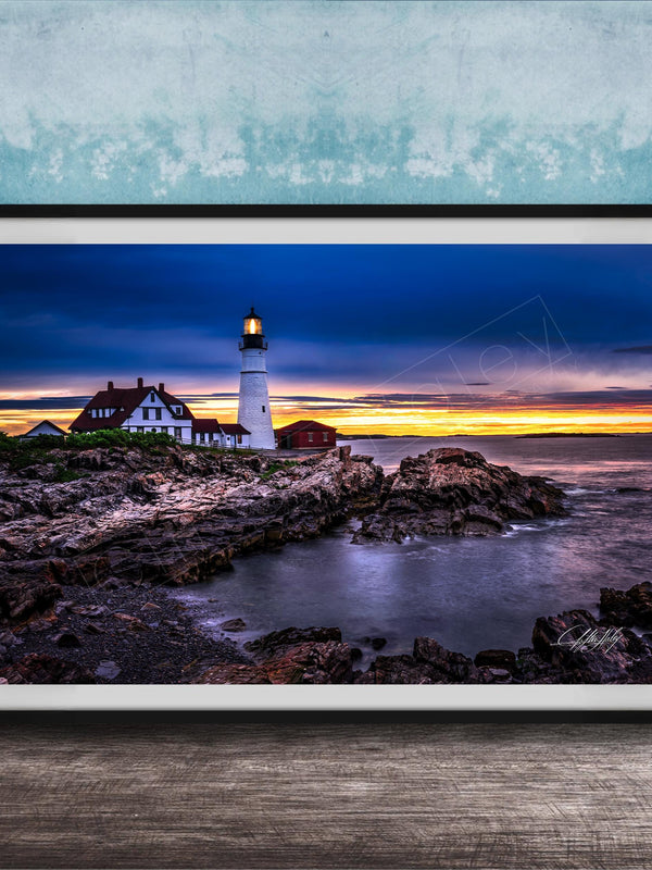 A framed photograph depicting a lighthouse on a rocky shore at sunset, with the sky filled with vibrant colors and the ocean reflecting the warm hues.