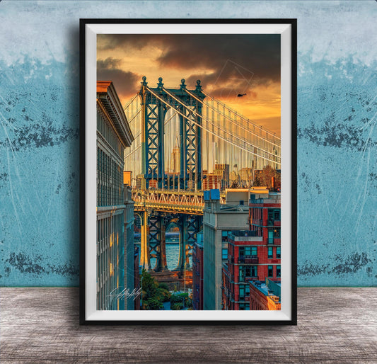 The image is a framed photograph of the Manhattan Bridge in New York City, with the bridge and surrounding buildings illuminated by a colorful sunset sky.