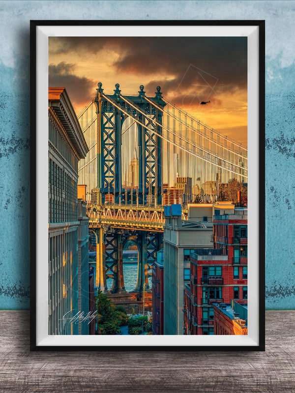 The image is a framed photograph of the Manhattan Bridge in New York City, with the bridge and surrounding buildings illuminated by a colorful sunset sky.