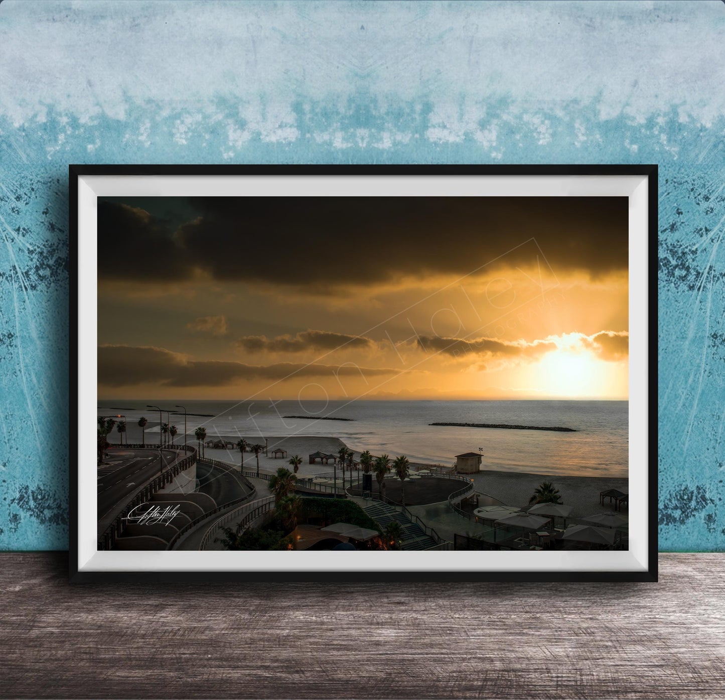 The image is a framed photograph of a beach at sunset, with palm trees and a body of water in the background.
